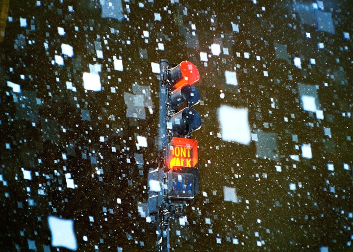 A traffic light with a "DONT WALK" signal is illuminated red amidst falling snow at night.