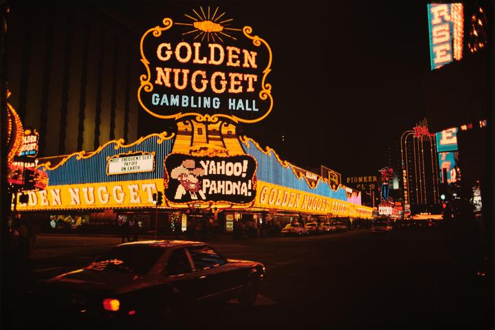 A street at night is illuminated by the neon signs of the Golden Nugget Gambling Hall and other casinos.