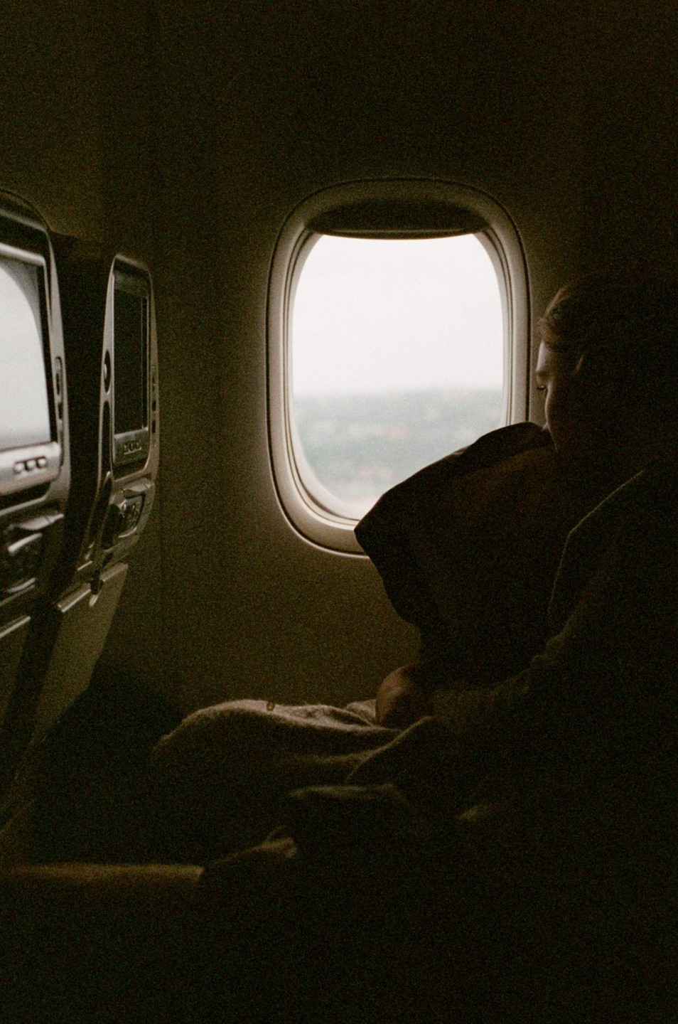 A person looks out an airplane window, with the cabin in shadow.