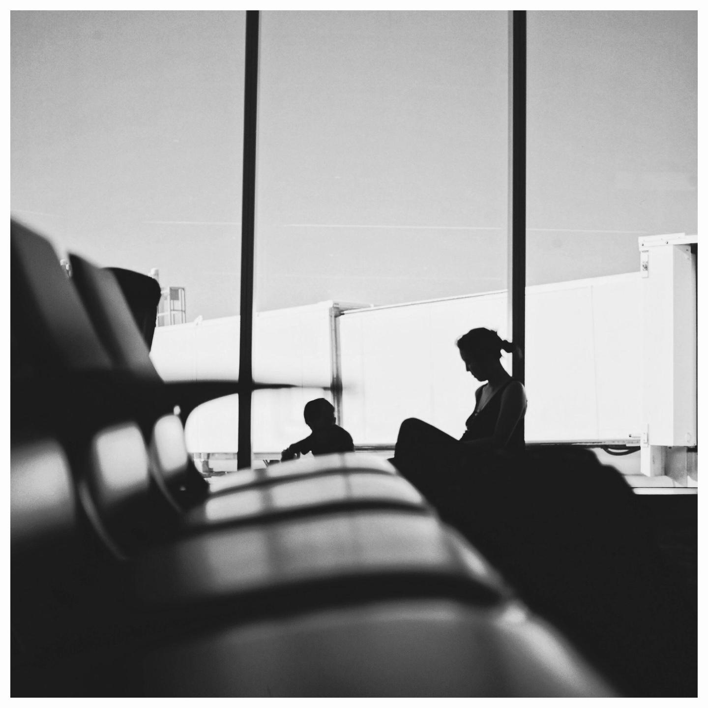A woman and child are silhouetted against a bright window in an airport waiting area.