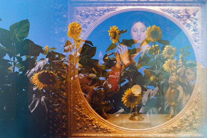 A double exposure shows sunflowers against a blue sky and a woman's face in an ornate mirror.