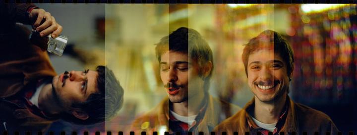 A man is depicted in a series of overlapping exposures, with one showing him holding a glass over his face and others showing him smiling and with his eyes closed.