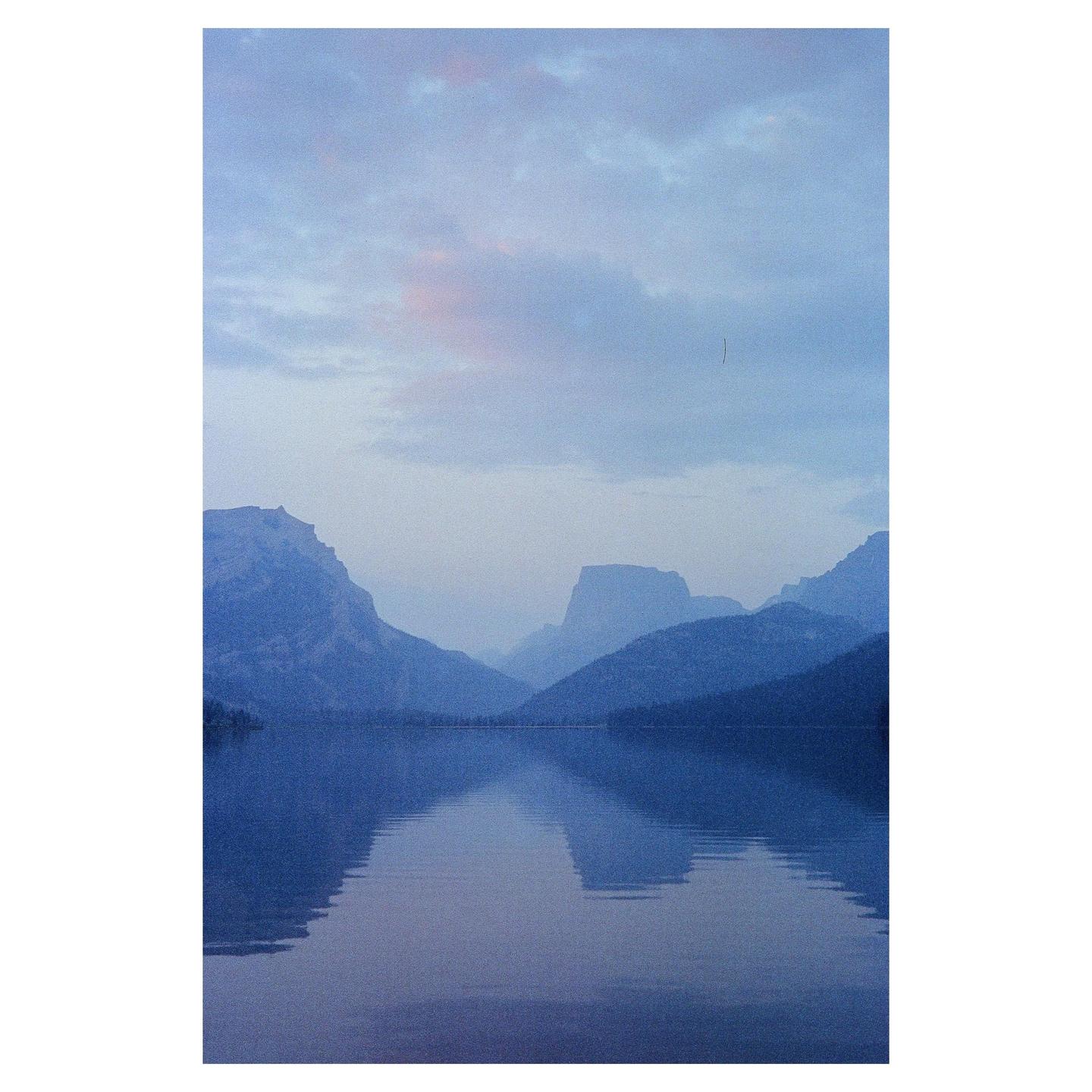 A calm lake reflects the mountains and sky at dusk.