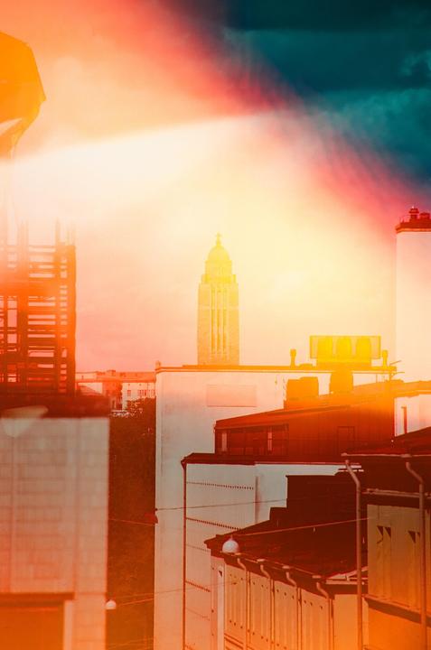 A tall, ornate tower rises above a city skyline, with a bright, colorful sky overhead.