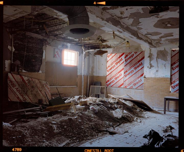 A large pile of debris sits on the floor of a derelict room with exposed brick, peeling paint, and a window.
