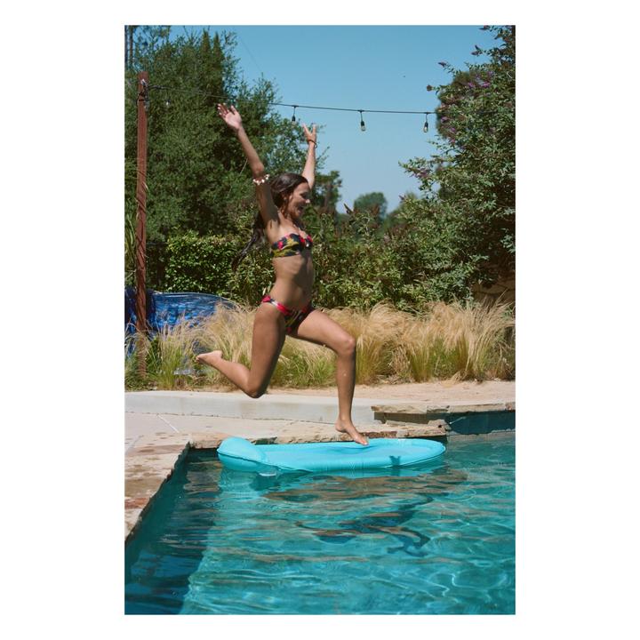 A woman in a bikini jumps into a swimming pool from the edge.