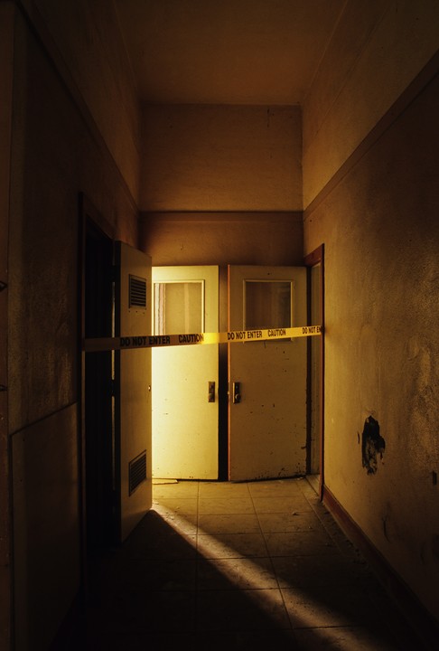 A yellow "Do Not Enter" tape is stretched across two doors in a dark hallway.