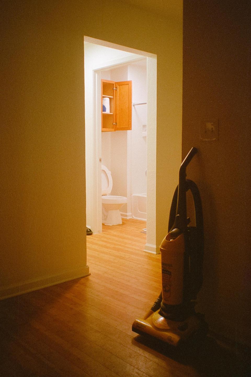A vacuum cleaner stands in a hallway with a bathroom visible through an open doorway.