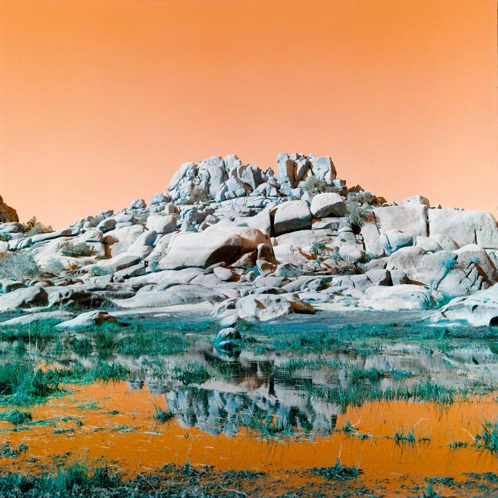 A rocky hill is reflected in a body of water with green grass.
