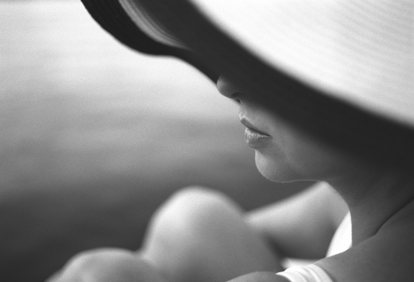 A woman's face is partially obscured by the shadow of a wide-brimmed hat.