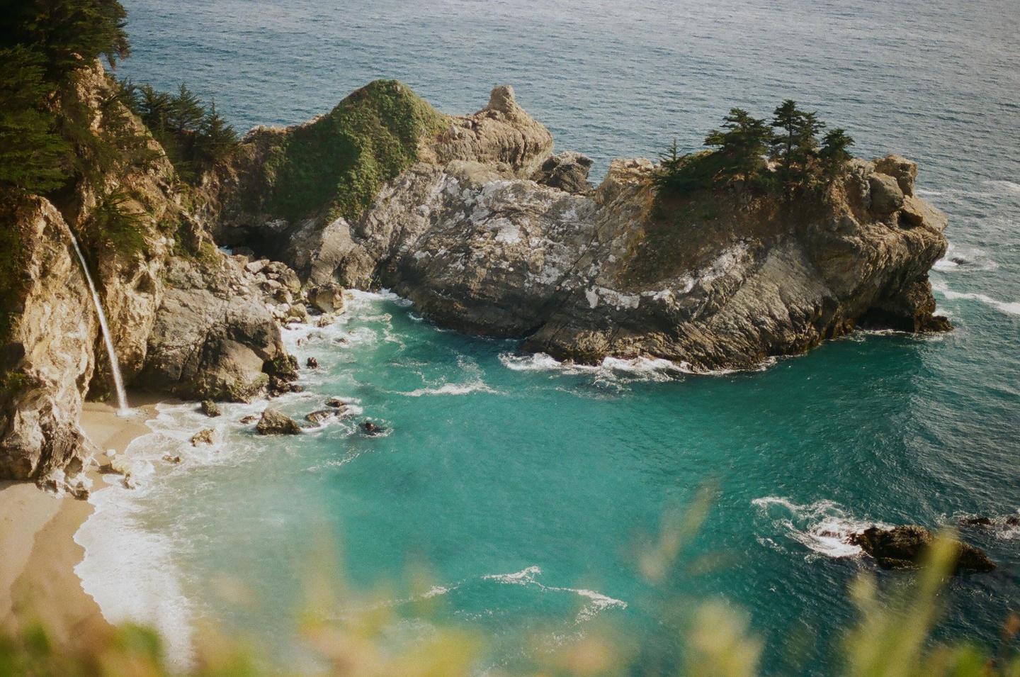 A waterfall cascades onto a sandy beach next to a rocky coastline with turquoise water.