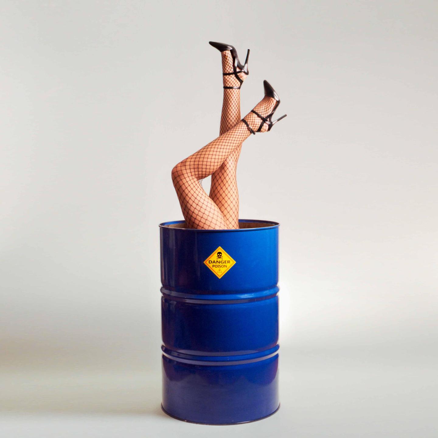 A pair of legs in fishnet stockings and high heels are sticking out of a blue barrel with a "danger poison" label.