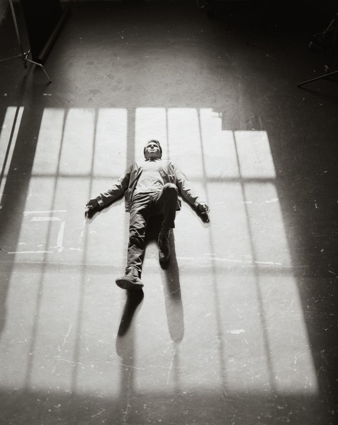 A man lies on a concrete floor with window shadows cast over him.