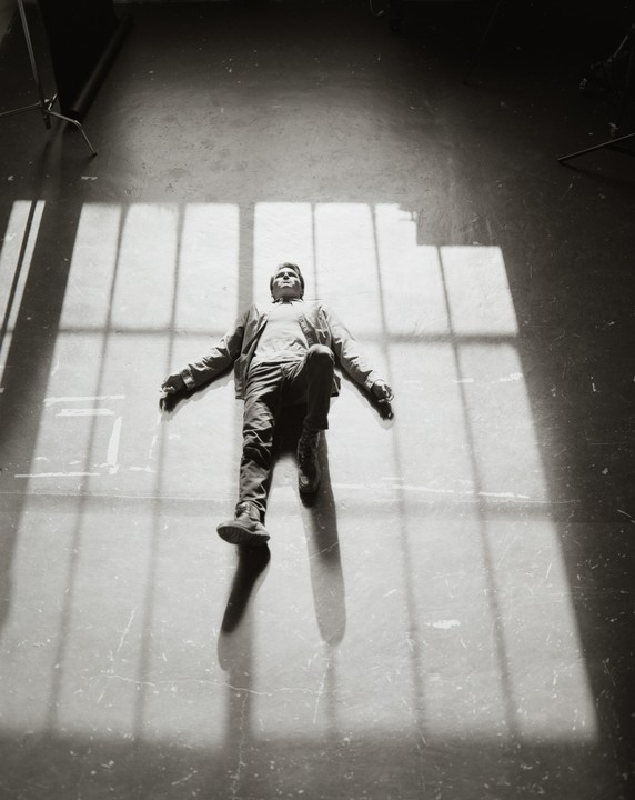 A man lies on a concrete floor with window shadows cast over him.