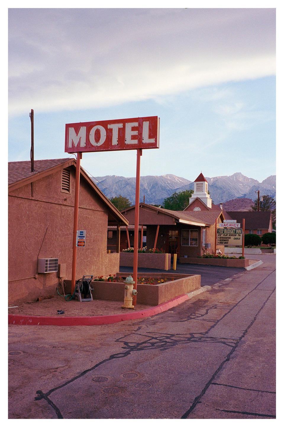 A red motel sign stands in front of a building with mountains in the background.