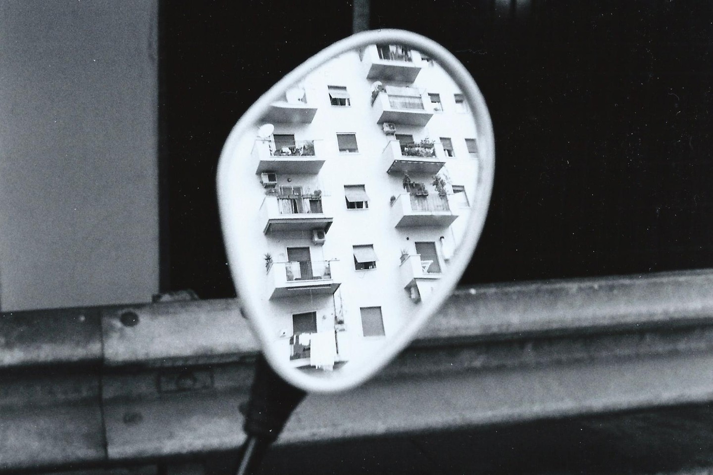 A building with balconies is reflected in a motorcycle mirror.