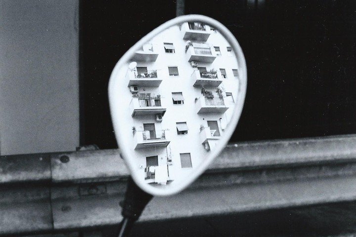 A building with balconies is reflected in a motorcycle mirror.