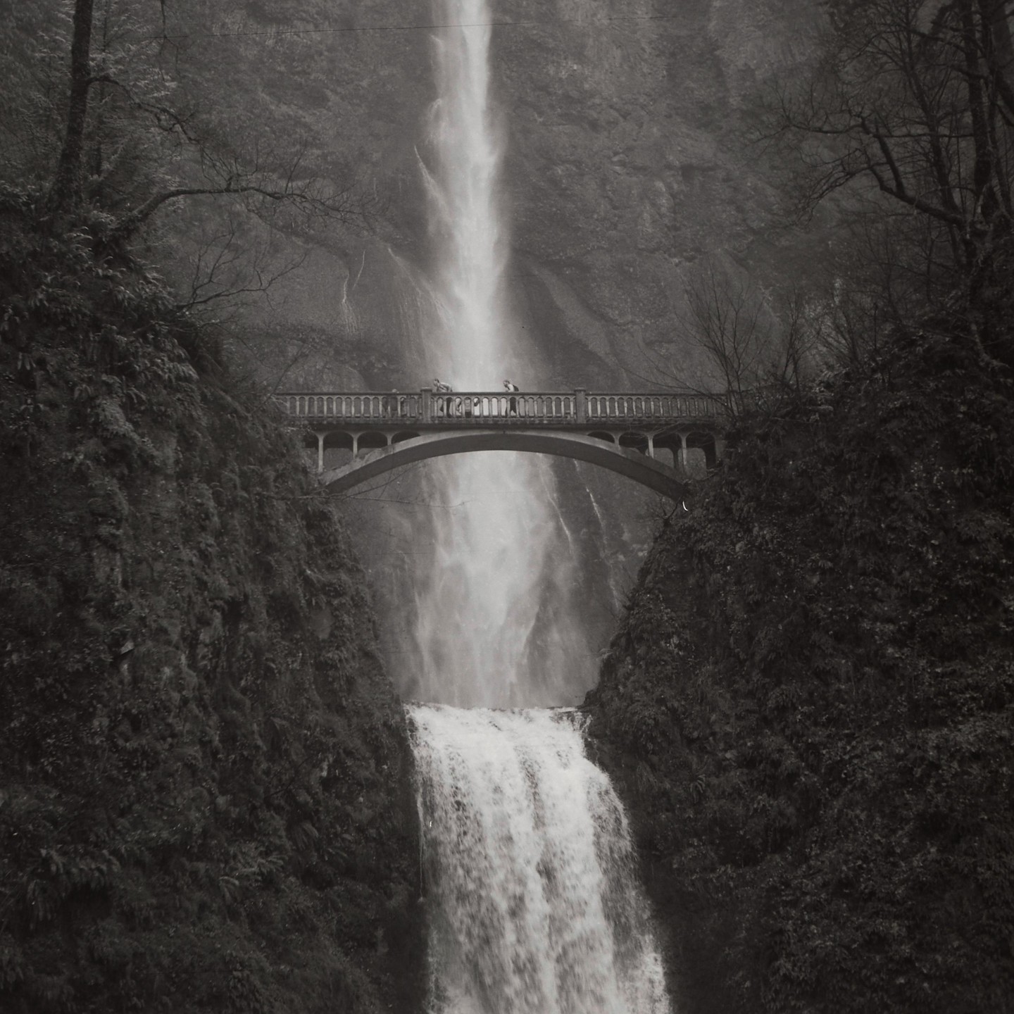 A bridge spans a tall waterfall with people standing on the bridge.