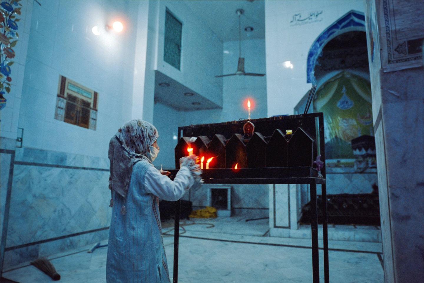A woman lights candles in a dimly lit room with marble walls and religious decorations.
