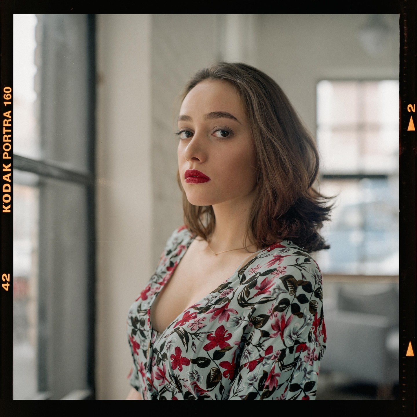 A woman with red lipstick and a floral dress looks towards the viewer.