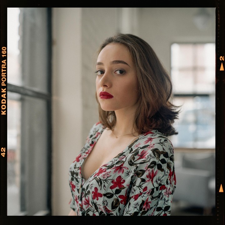 A woman with red lipstick and a floral dress looks towards the viewer.