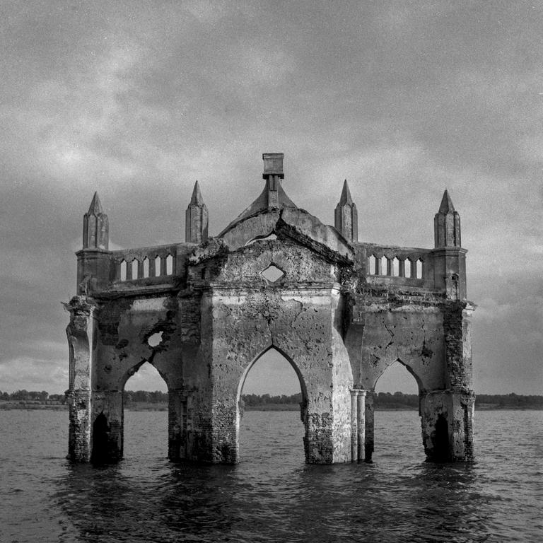 A ruined church stands in a body of water under a cloudy sky.