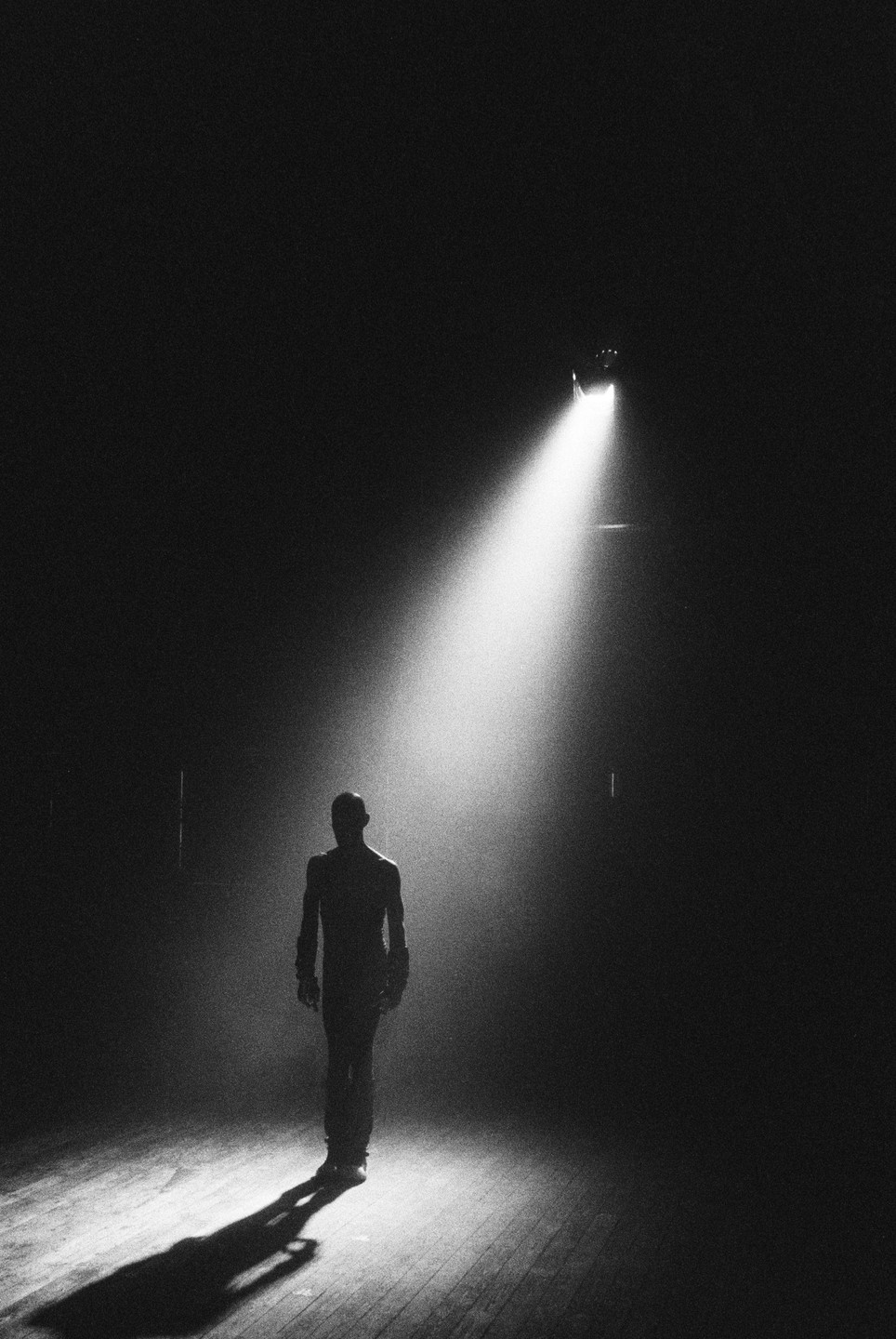 A man stands on a stage in a spotlight, casting a long shadow.