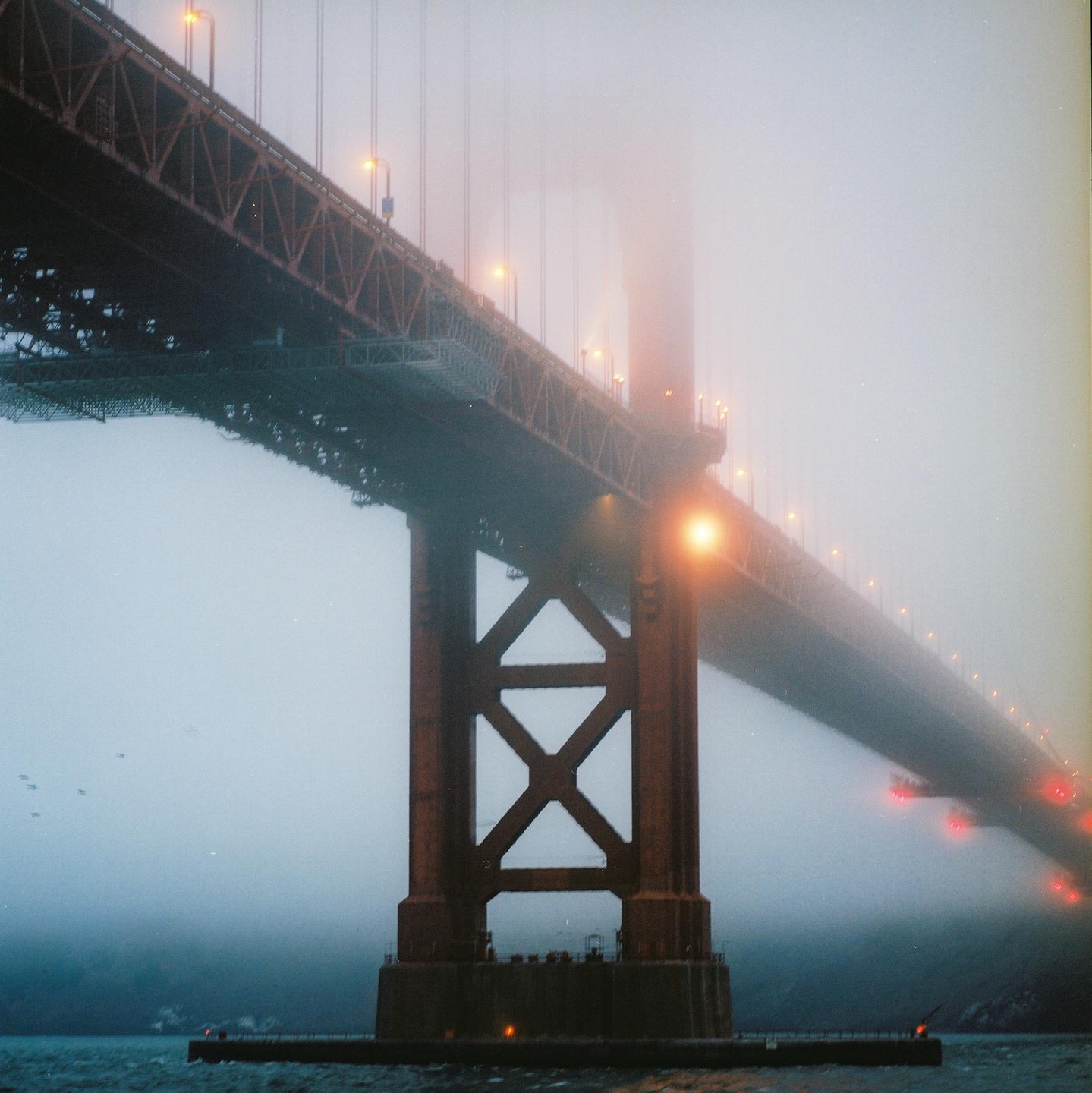 The Golden Gate Bridge is shrouded in fog, with its lights illuminating the mist.