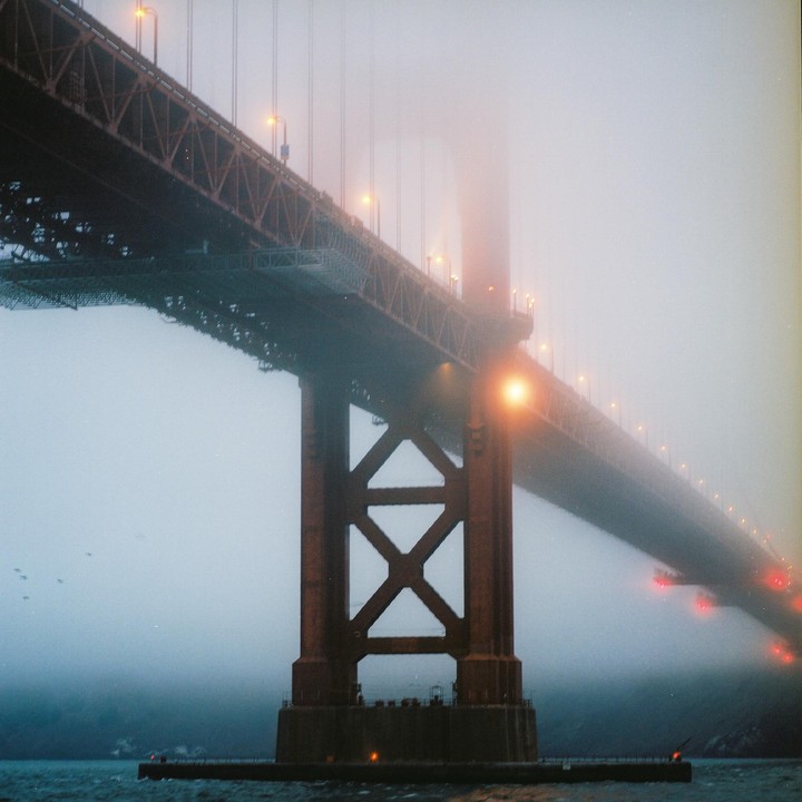 The Golden Gate Bridge is shrouded in fog, with its lights illuminating the mist.
