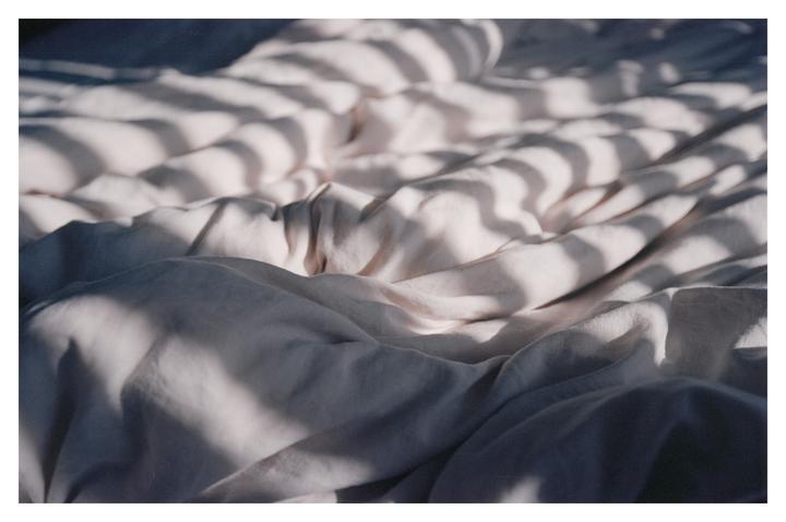 Sunlight casts striped shadows across rumpled bed sheets.