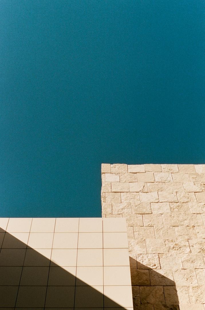 Two buildings with different textures meet under a clear blue sky, with shadows cast on their surfaces.