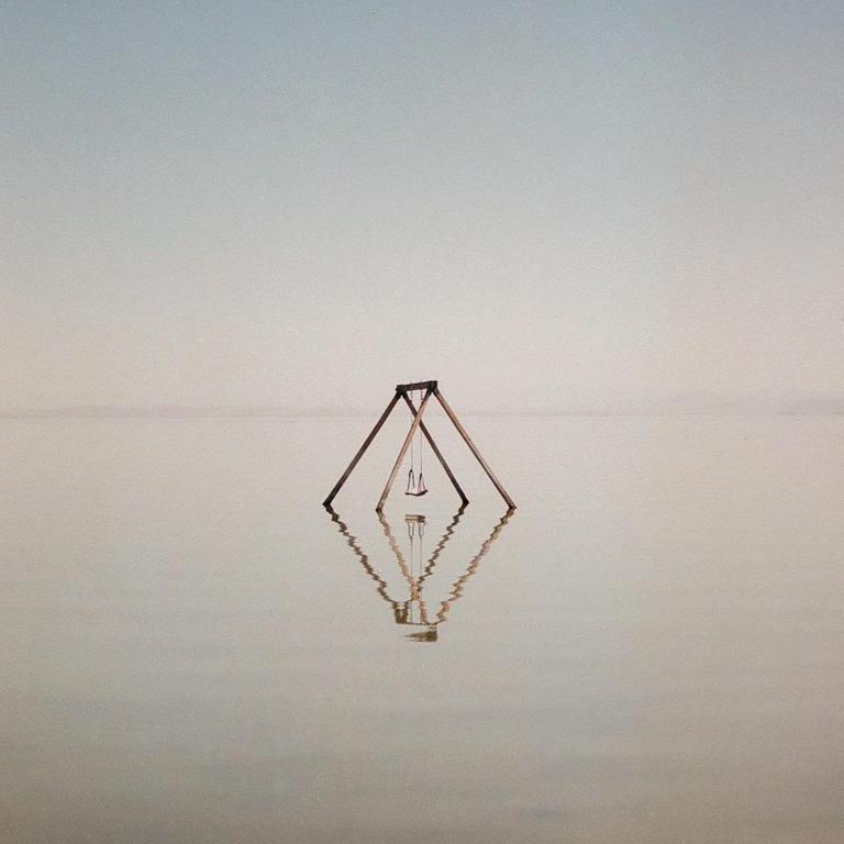 A swing set stands in the middle of a body of water, reflecting on the surface.