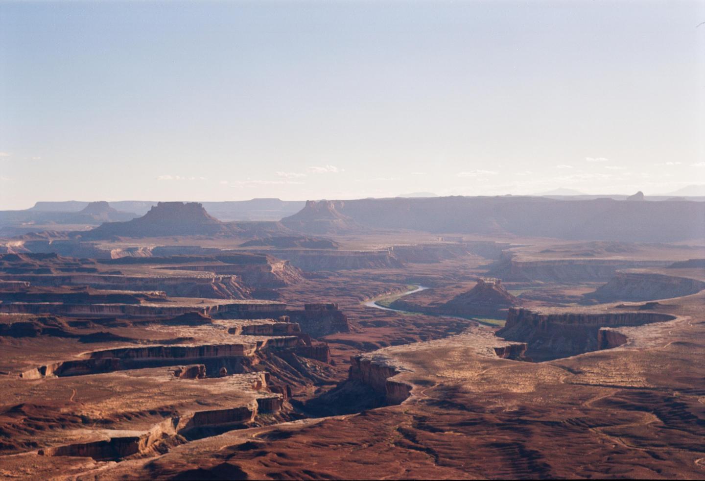 A wide landscape shows a winding river through a vast canyon under a clear sky.