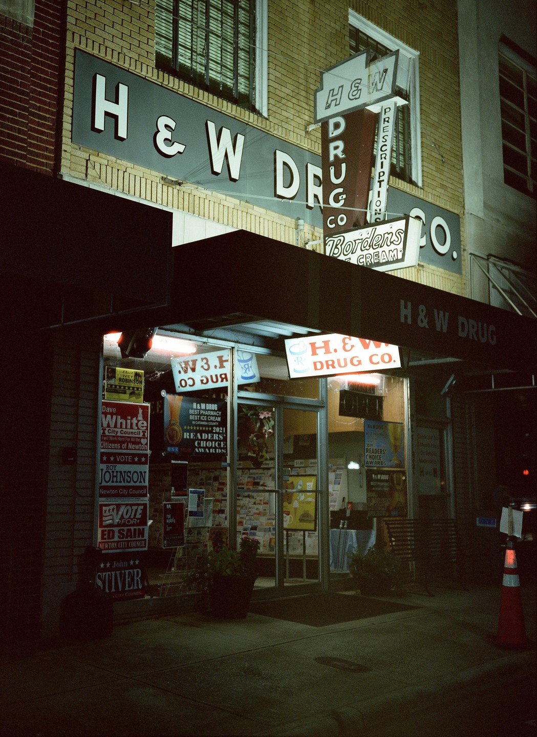 A drug store with a large sign and an awning is illuminated at night.