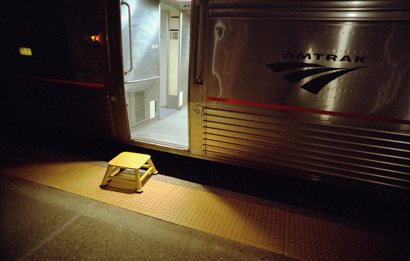 A yellow step stool sits on a train platform next to an open train door at night.