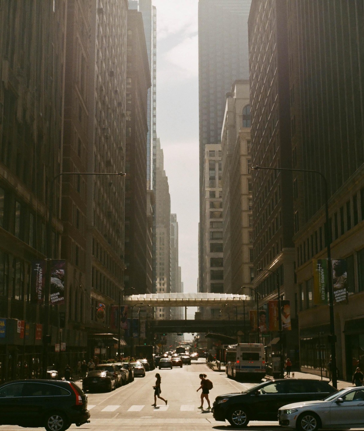 Two women cross a busy street in downtown Chicago, surrounded by tall buildings and cars.