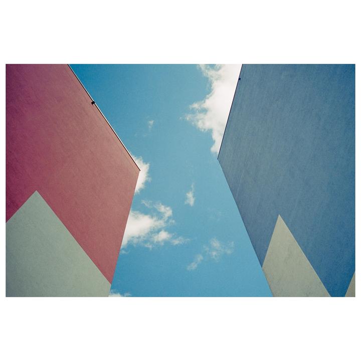 Two colorful building facades frame a bright blue sky with white clouds.