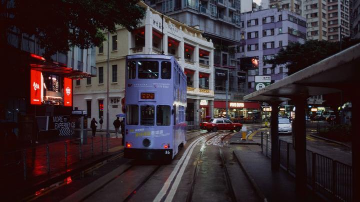 A purple double-decker tram travels on a wet street at night in a city.