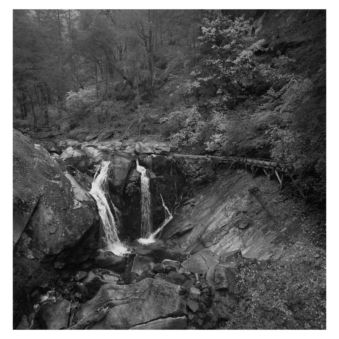 A waterfall cascades over rocks in a forest with a wooden structure built into the hillside.