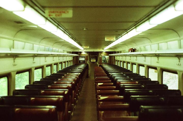 An empty train car with rows of seats on either side of an aisle is illuminated by overhead lights.