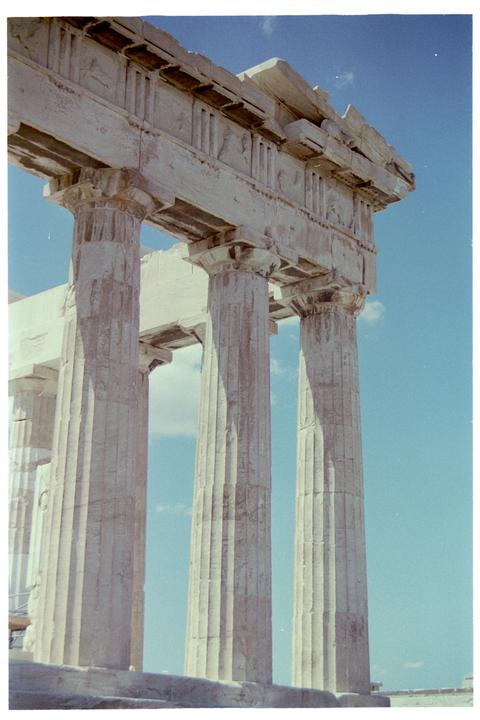 A low-angle view shows several large, fluted columns supporting a stone entablature against a clear blue sky.