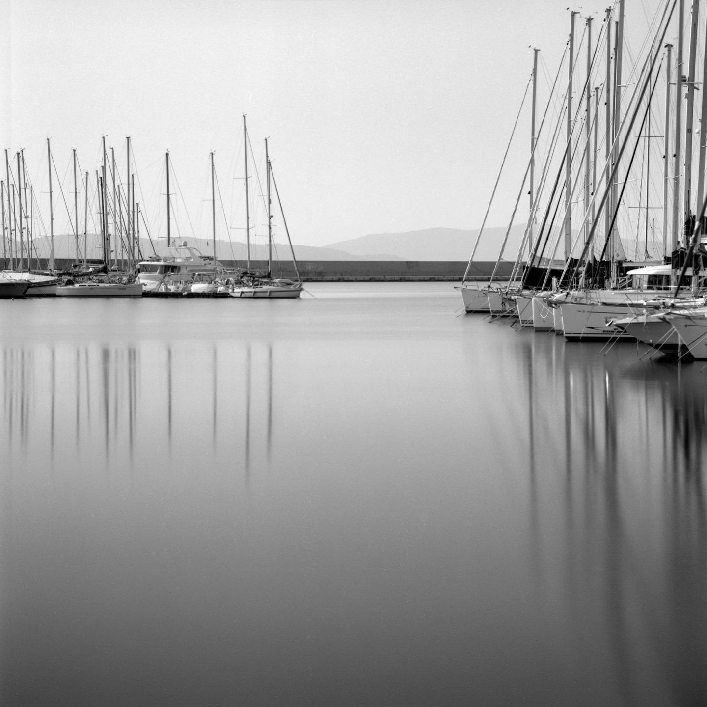 Sailboats are docked at a pier with mountains in the distance.