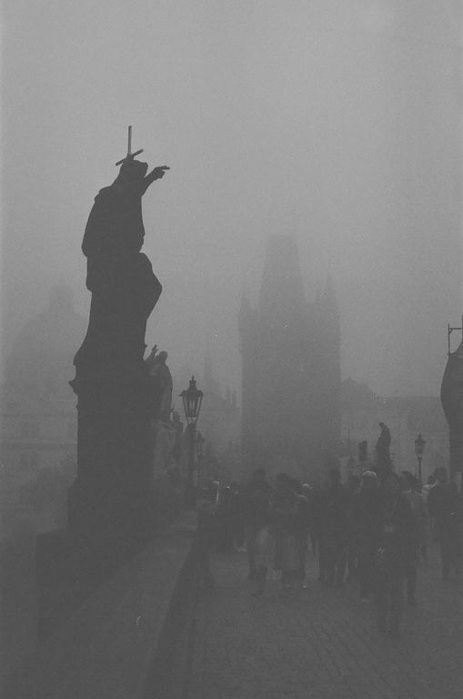 A statue stands on a bridge with people walking in the fog.