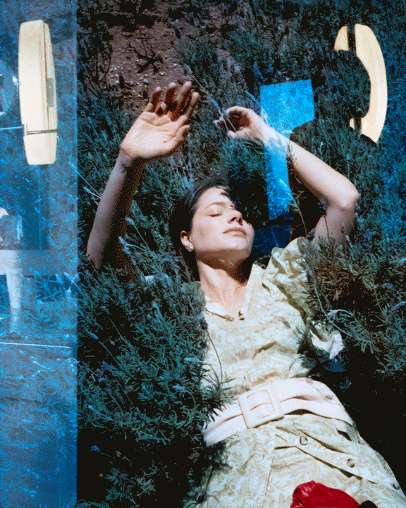 A woman in a patterned dress lies in green foliage with her eyes closed, with a blue overlay and outlines of a telephone receiver.
