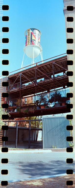 A water tower with a colorful mural stands above a multi-story building with plants on its balconies.