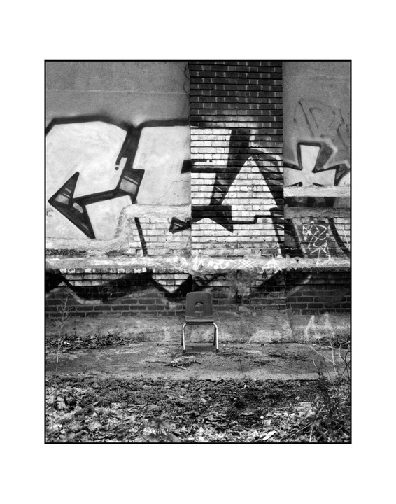 A single chair sits in front of a brick wall covered in graffiti.