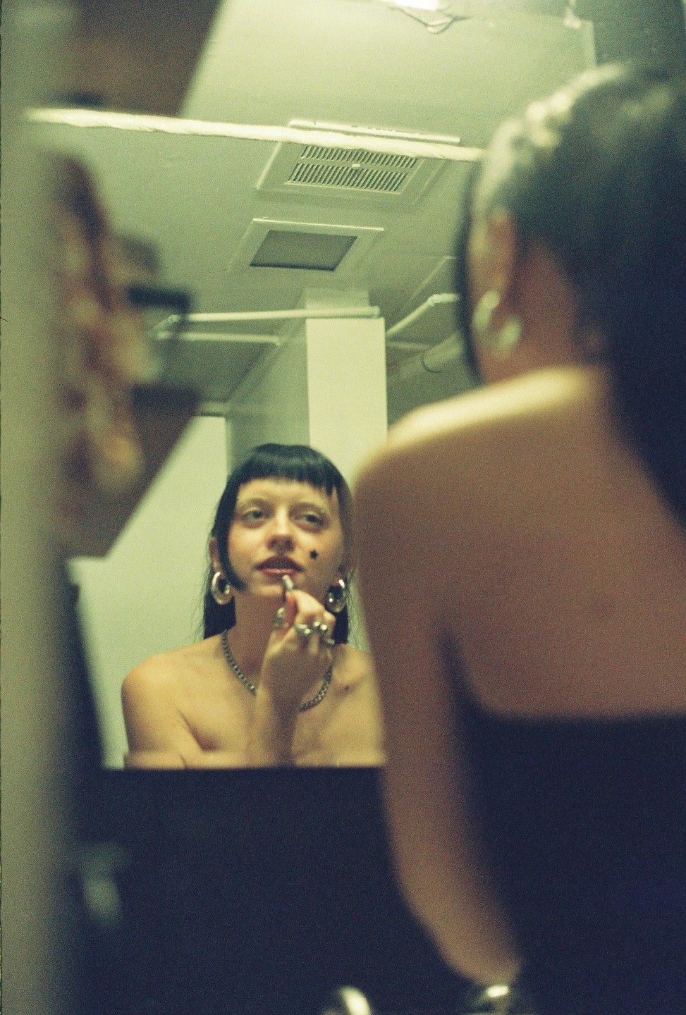 A woman applies lipstick while looking at her reflection in a mirror.