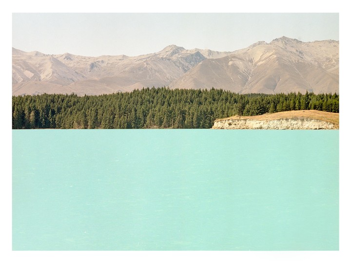 A turquoise lake is in the foreground, with a forest and mountains in the background.