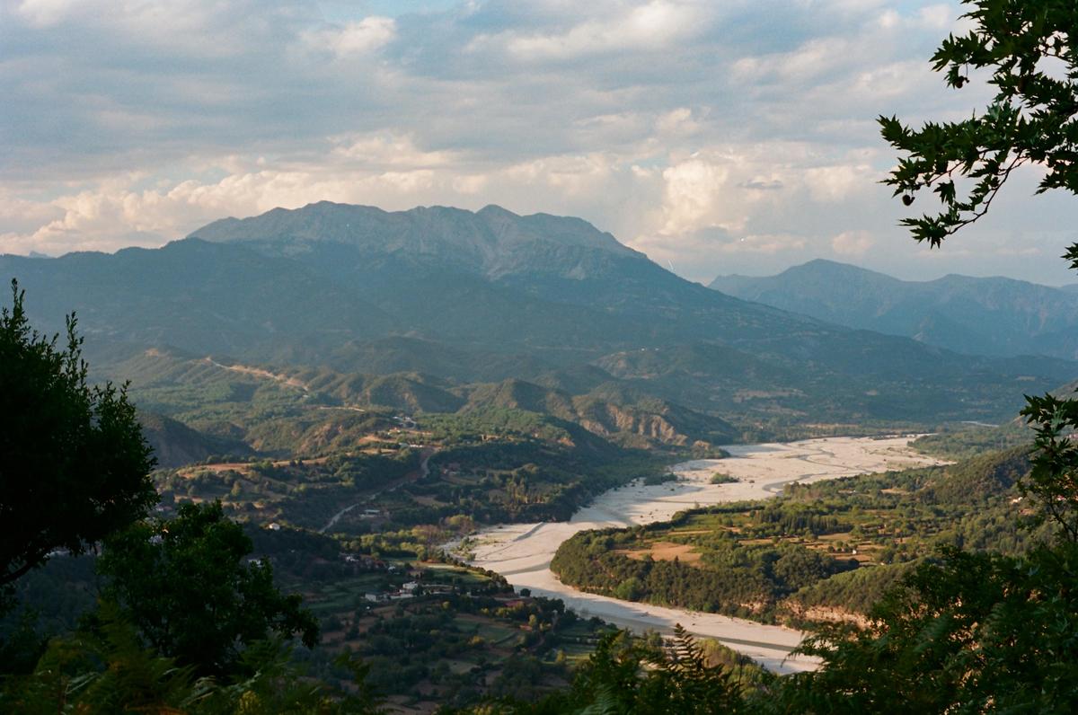 A wide river flows through a valley surrounded by mountains under a cloudy sky.
