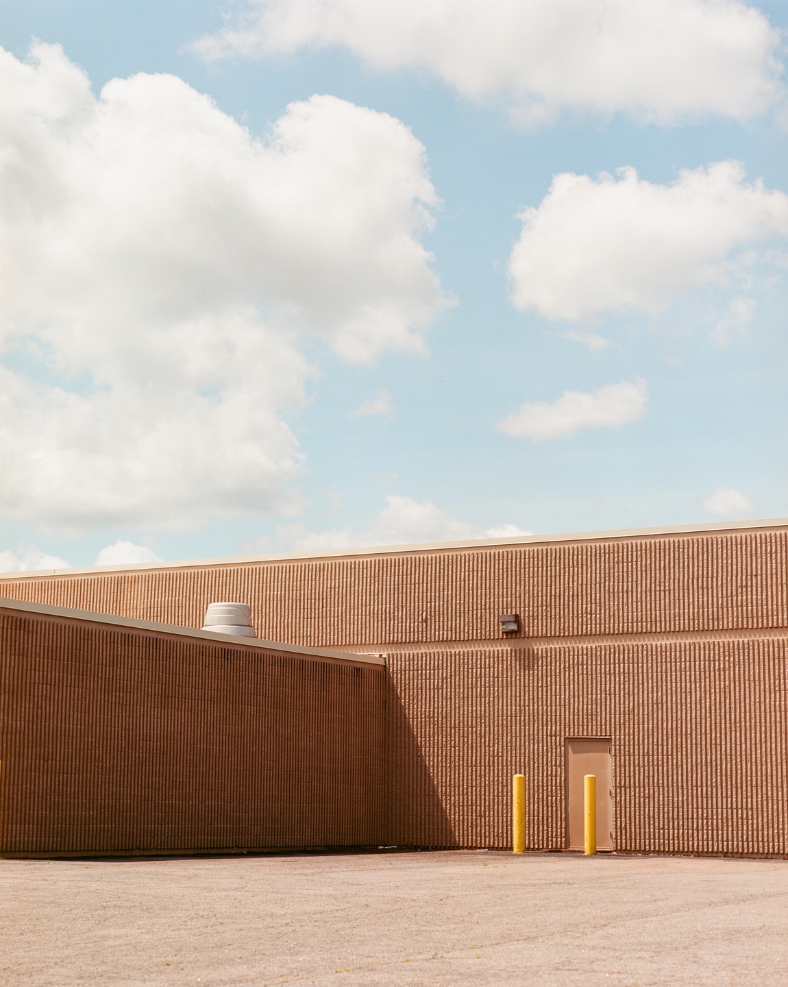 A building with textured walls and a light-colored door is visible under a blue sky with white clouds.